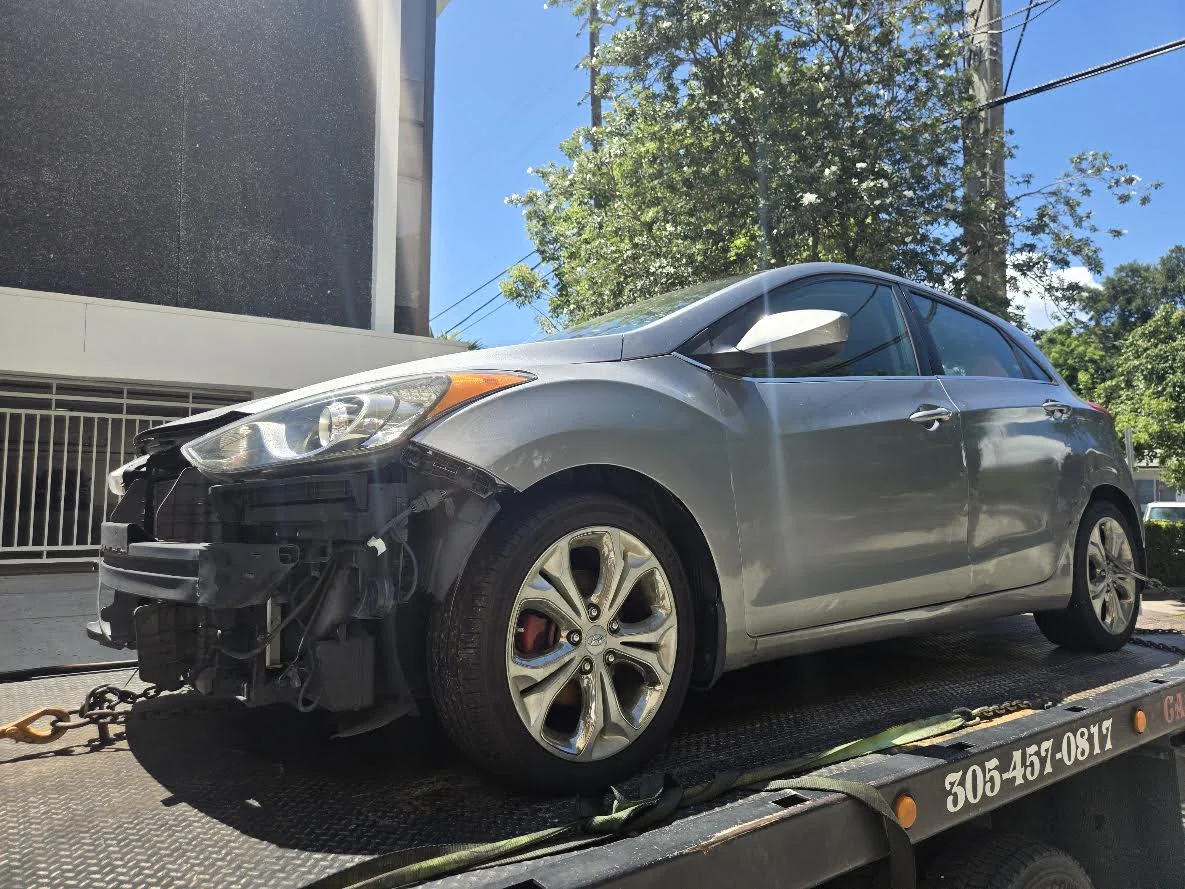 Damaged gray car secured on a Cash 4 Junk Cars Miami flatbed truck
