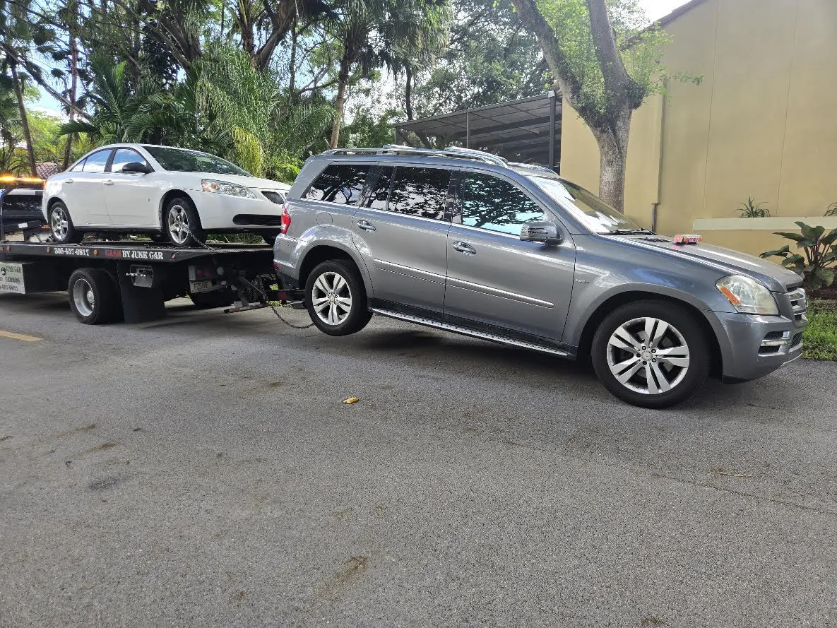Real flatbed tow truck carrying a white Pontiac sedan as a junk car pickup example for Kendall