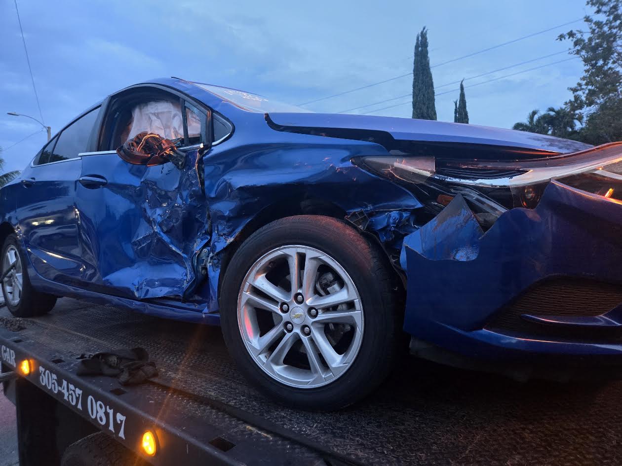 Severely damaged blue car secured on a flatbed in Miami-Dade